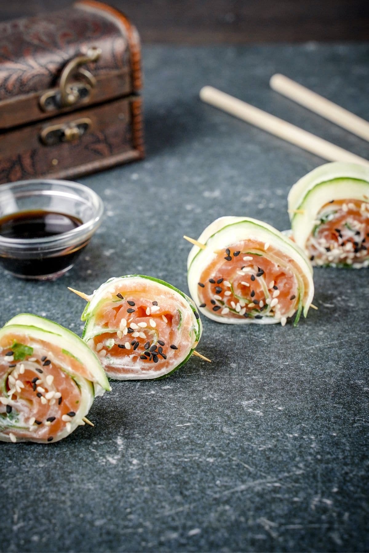 rolled cucumber slices with salmon and black sesames on black table with chopsticks in the background