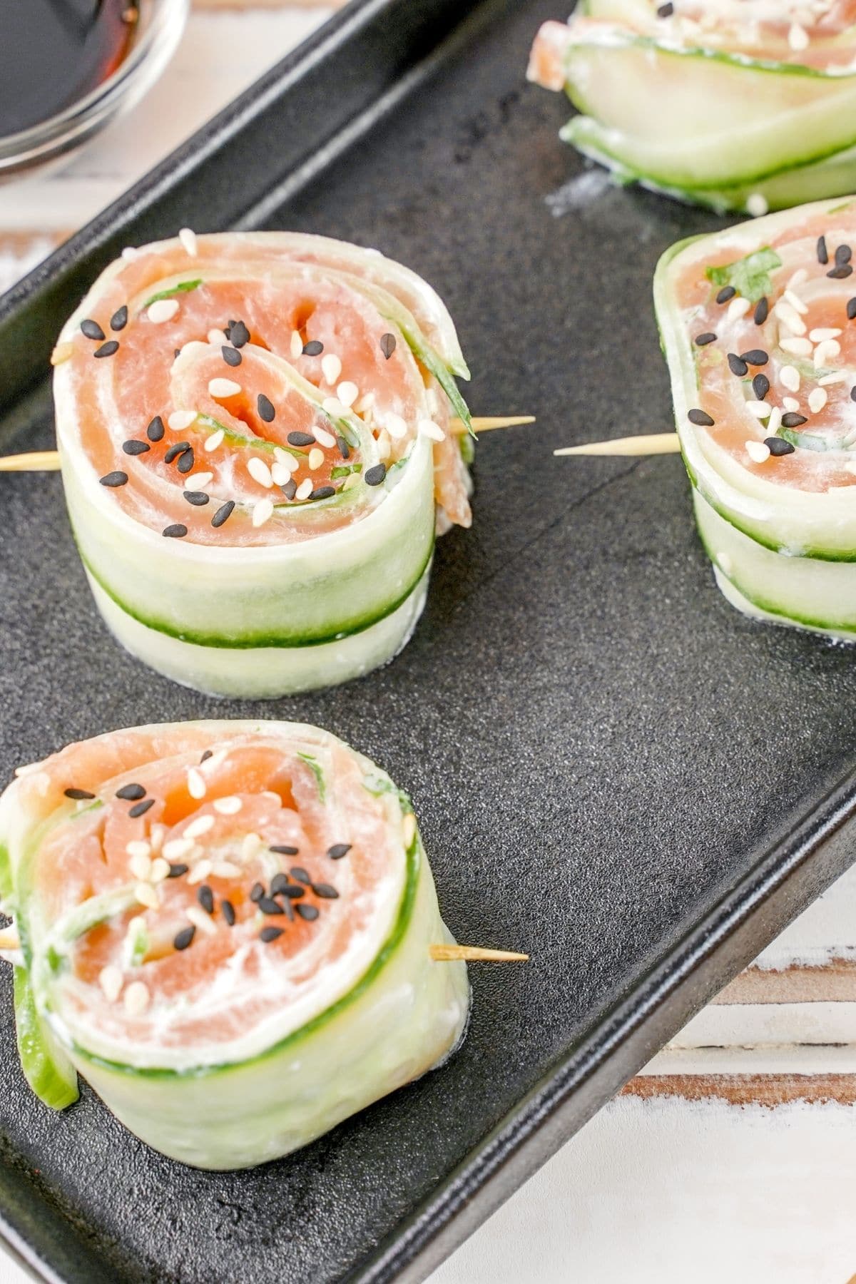 four cucumber smoked salmon rolls on black plate sitting on wood table
