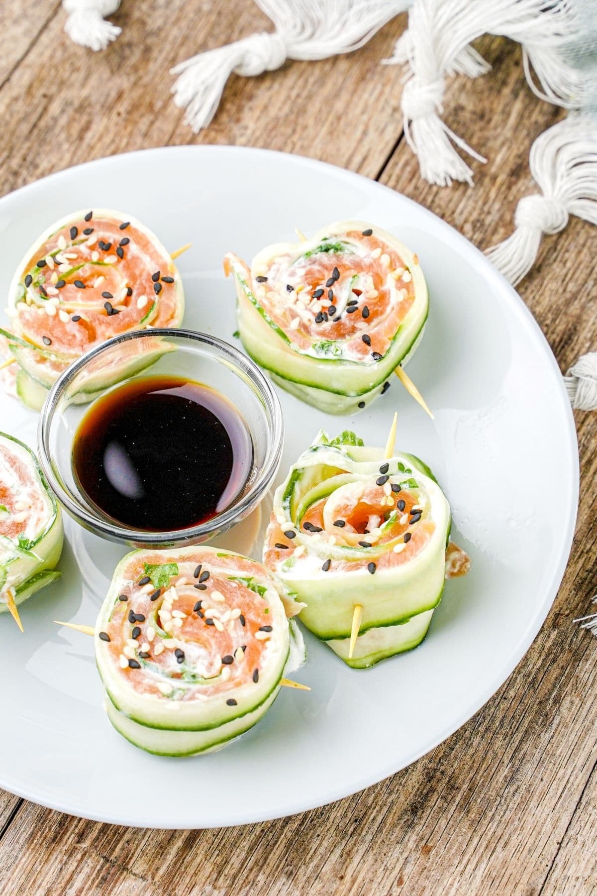 cucumber rolls held together by toothpicks on white plate with small glass bowl of soy sauce in center of plate