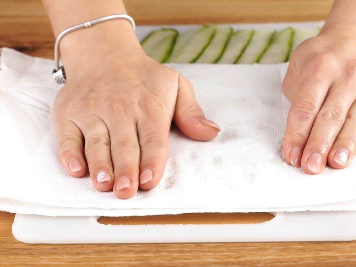 hand patting paper towel over top of cucumber slices