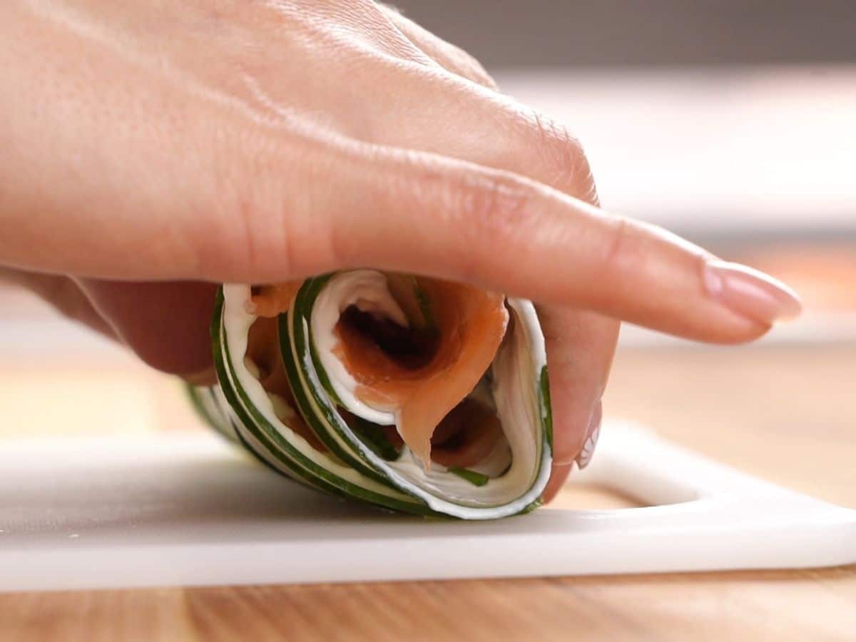 hand rolling cucumber and salmon into sushi on white cutting board