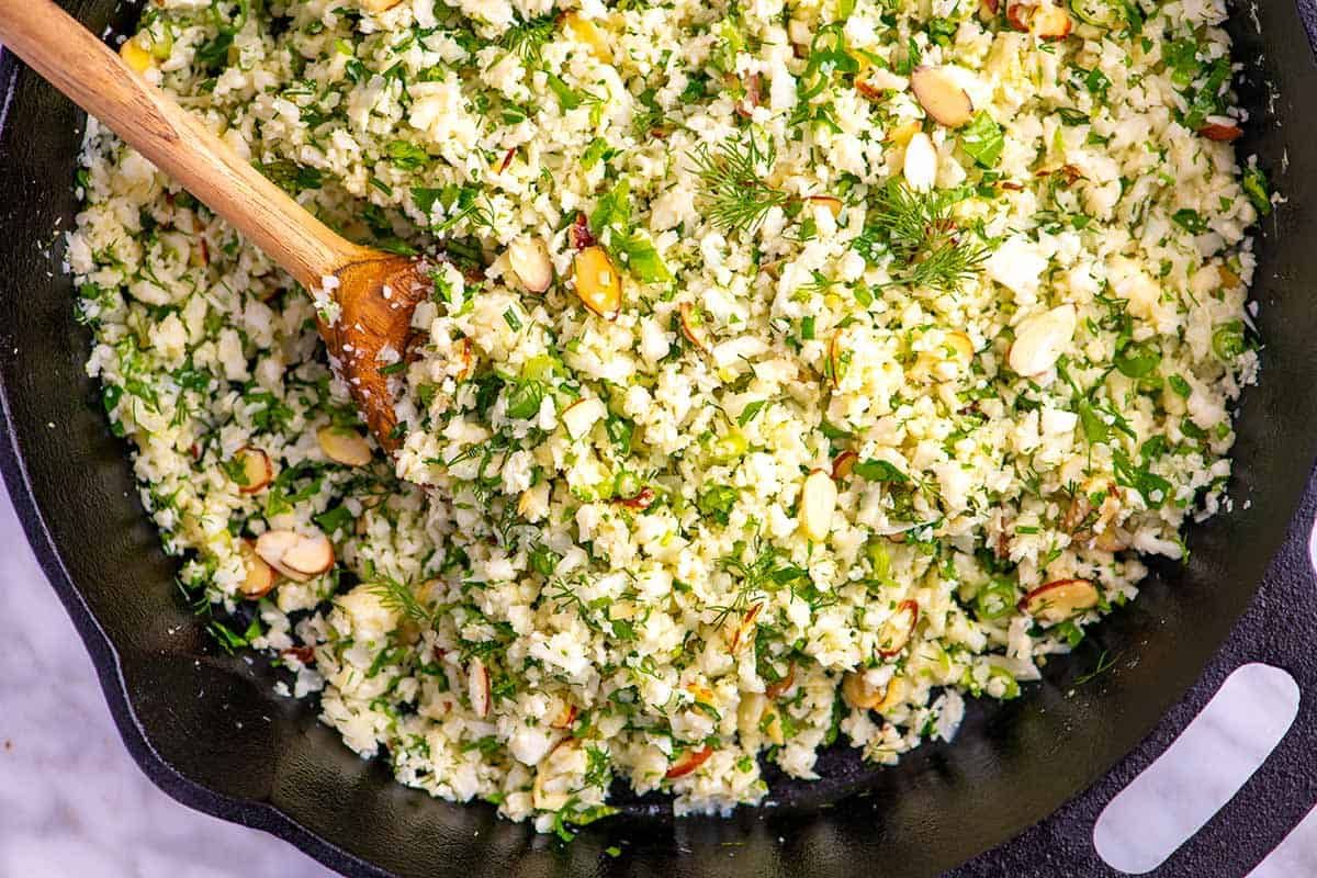 skillet of cauliflower rice with herbs and wooden spoon