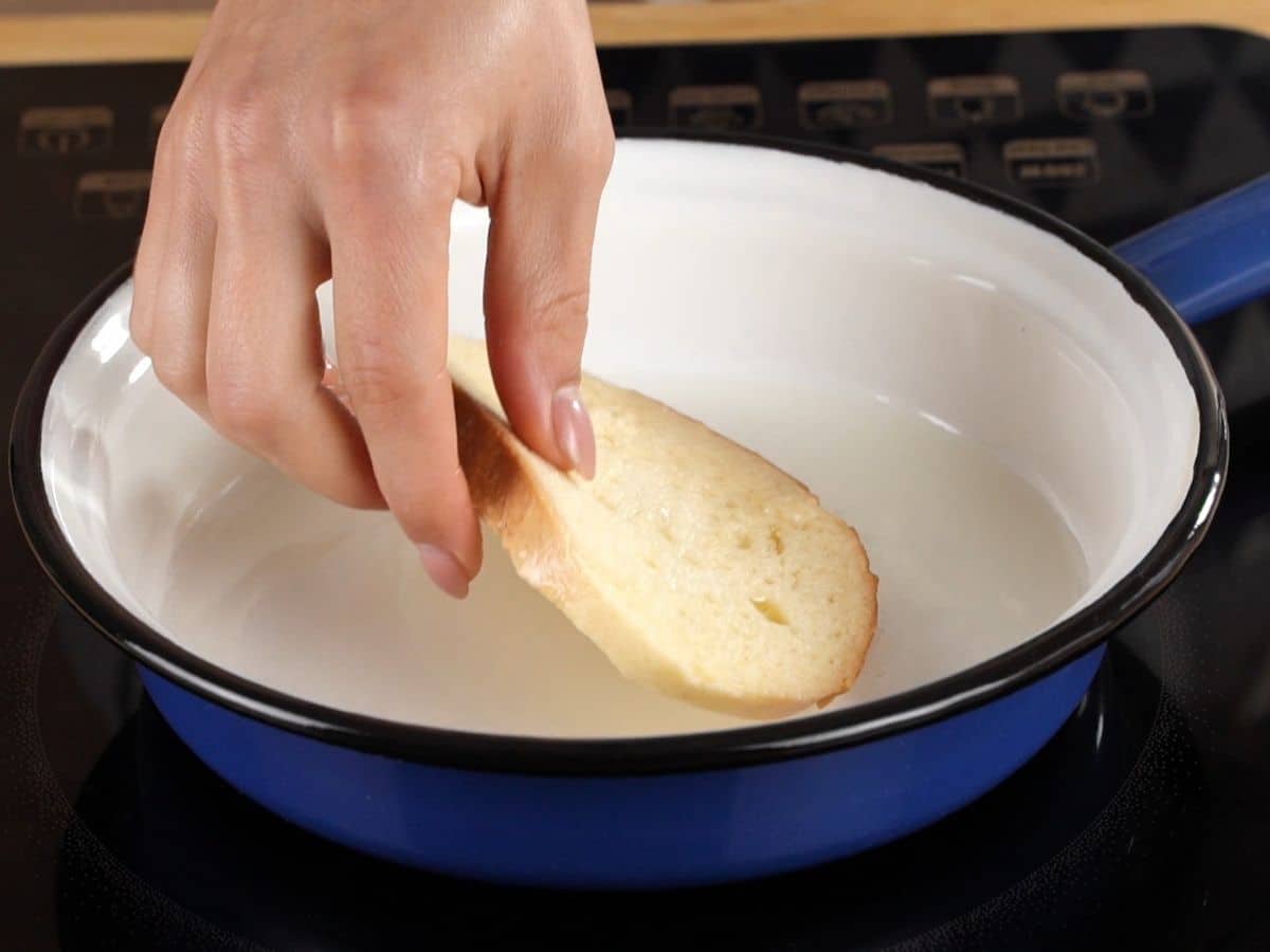 hand placing bread into white and blue skillet