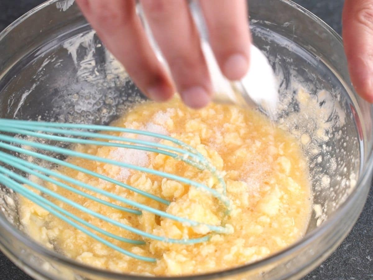 hand pouring sugar into egg and butter mixture in glass bowl
