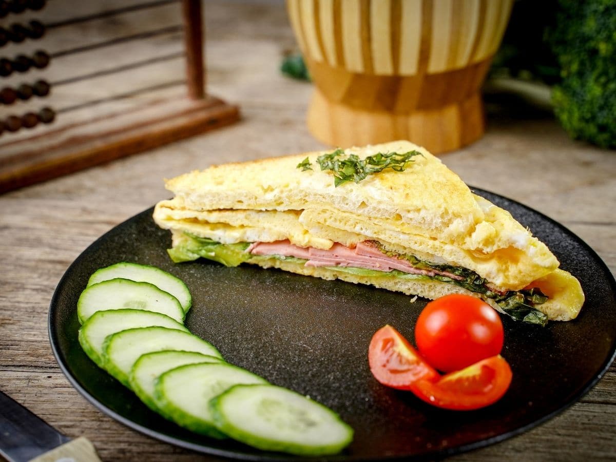 egg and ham sandwich on black plate with cucumber and tomato slices