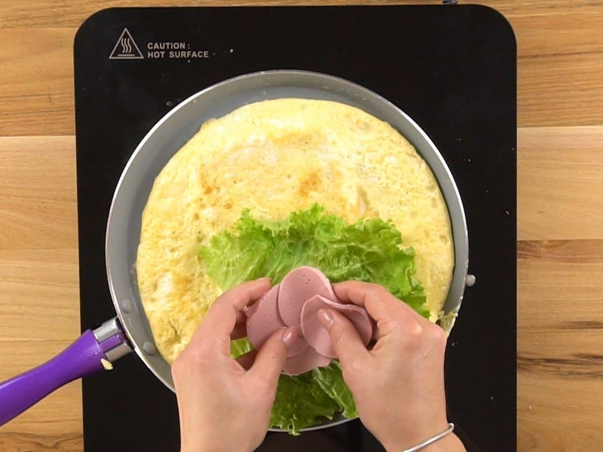 hands placing ham on lettuce in egg