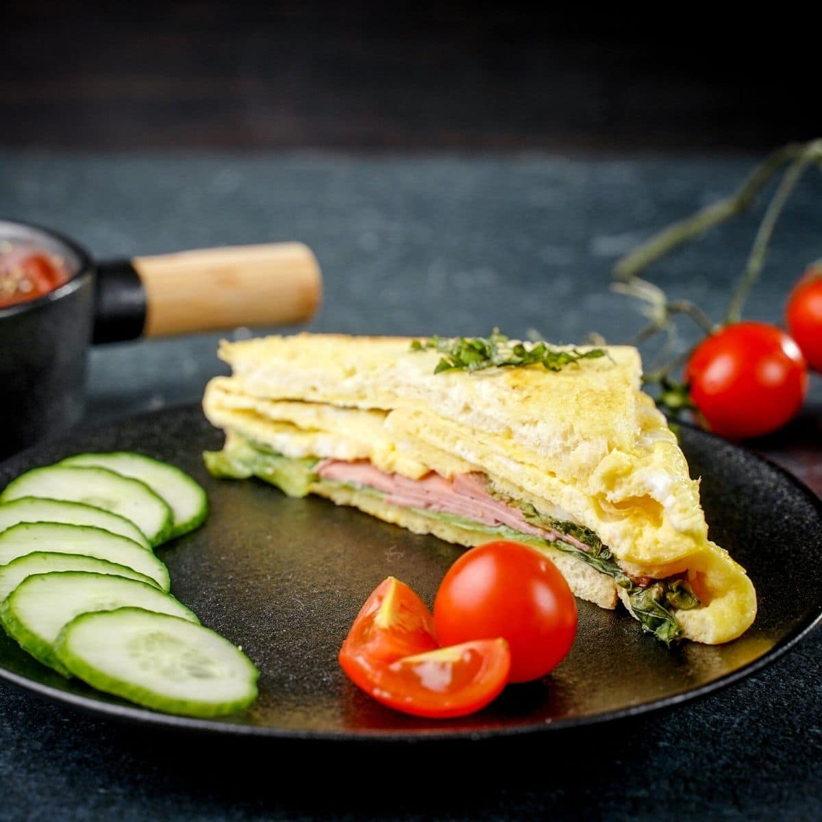egg sandwich on black plate with tomato and cucumber