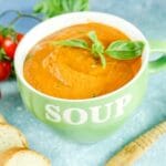light green bowl that says soup filled with tomato Boursin soup sitting on blue table