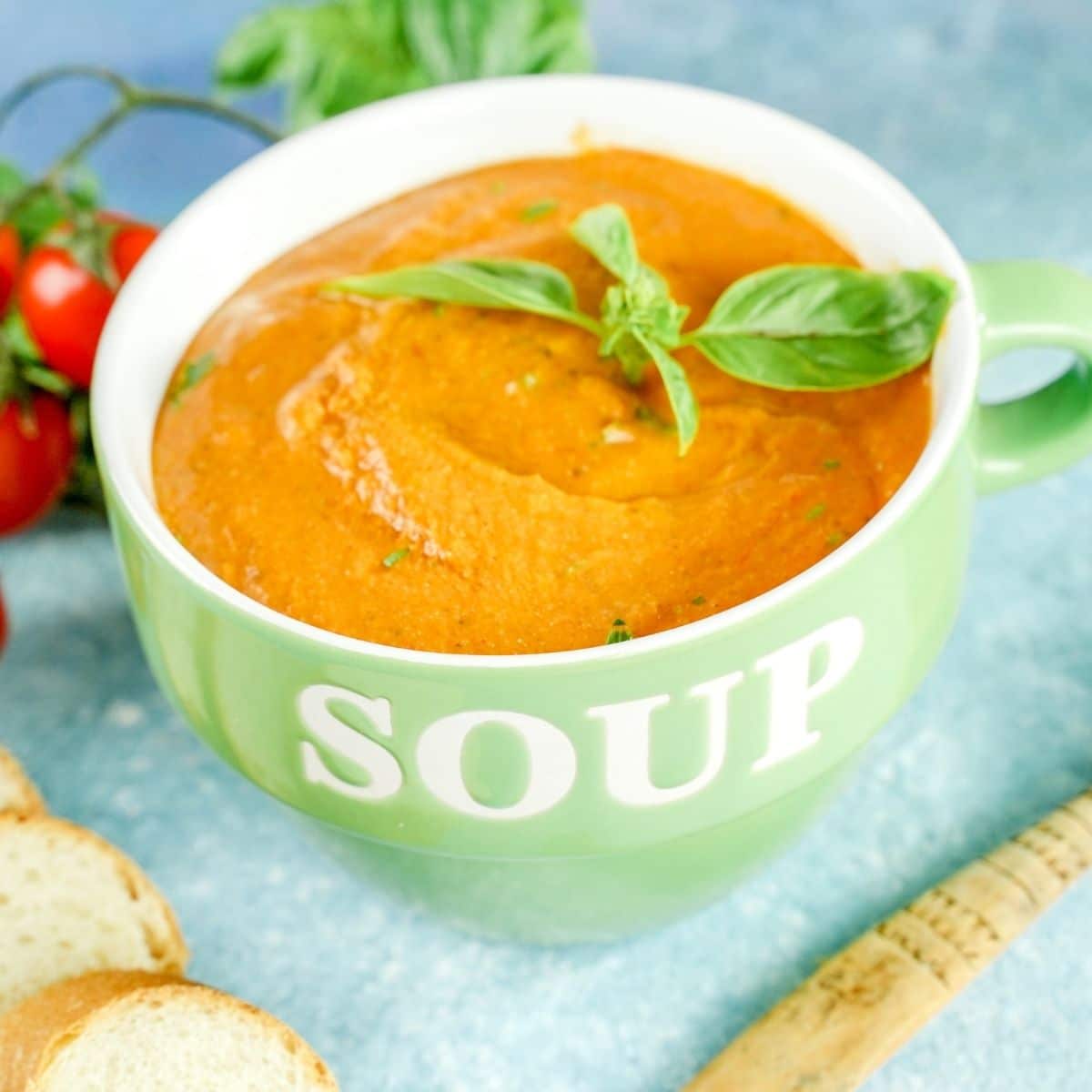 light green bowl that says soup filled with tomato Boursin soup sitting on blue table