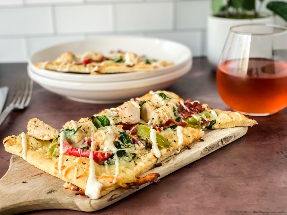 chicken bacon ranch flatbread pizza on cutting board by glass of wine