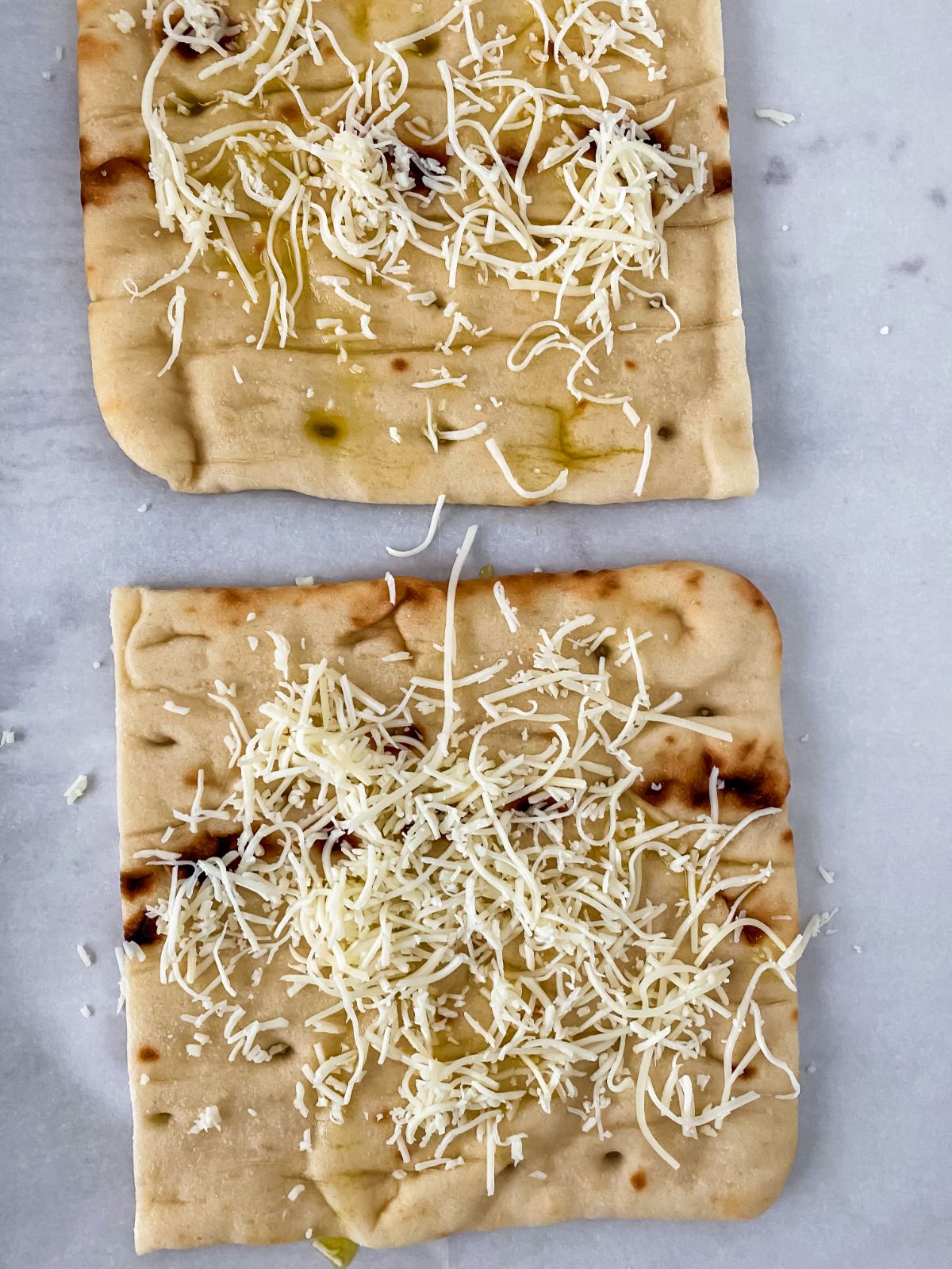 two flatbreads topped with cheese on parchment paper