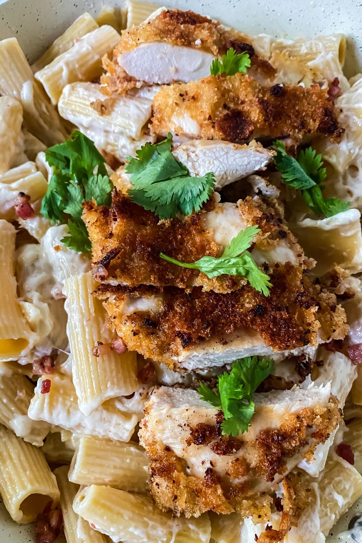 sliced fried chicken on top of pasta with parsley on top