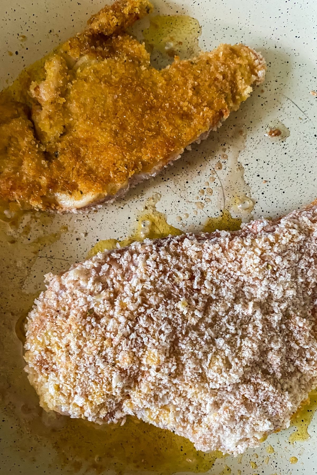 chicken breasts in skillet with one cooked and the second raw