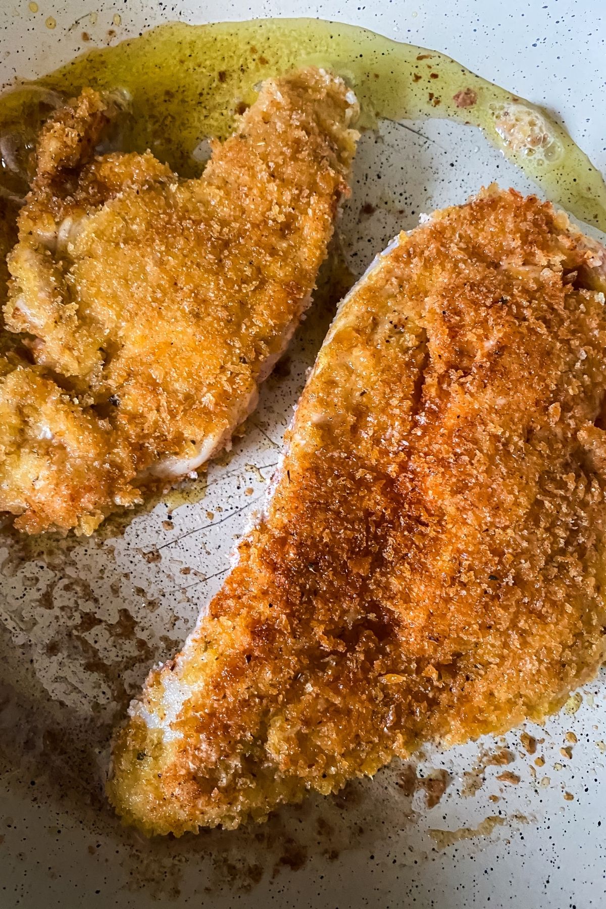 two browned chicken breasts in white skillet