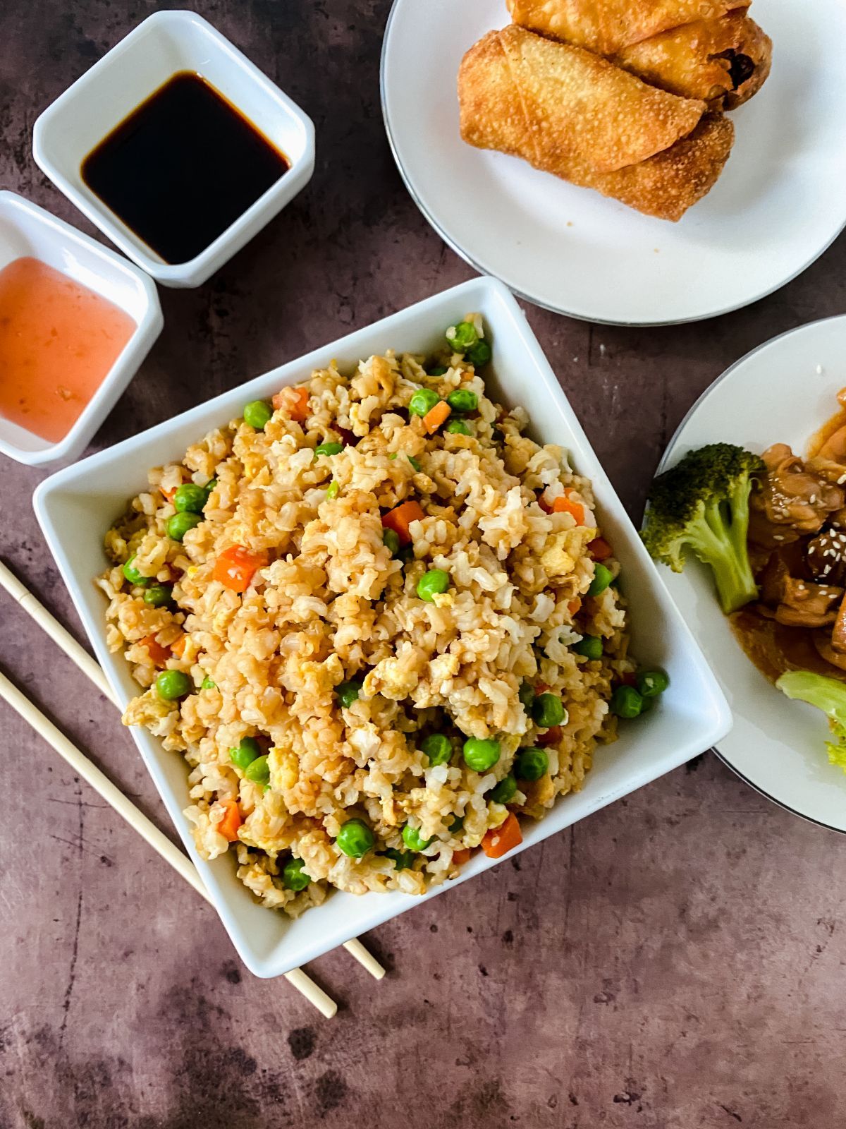 square white bowl of fried rice next to saucers of chicken and vegetables