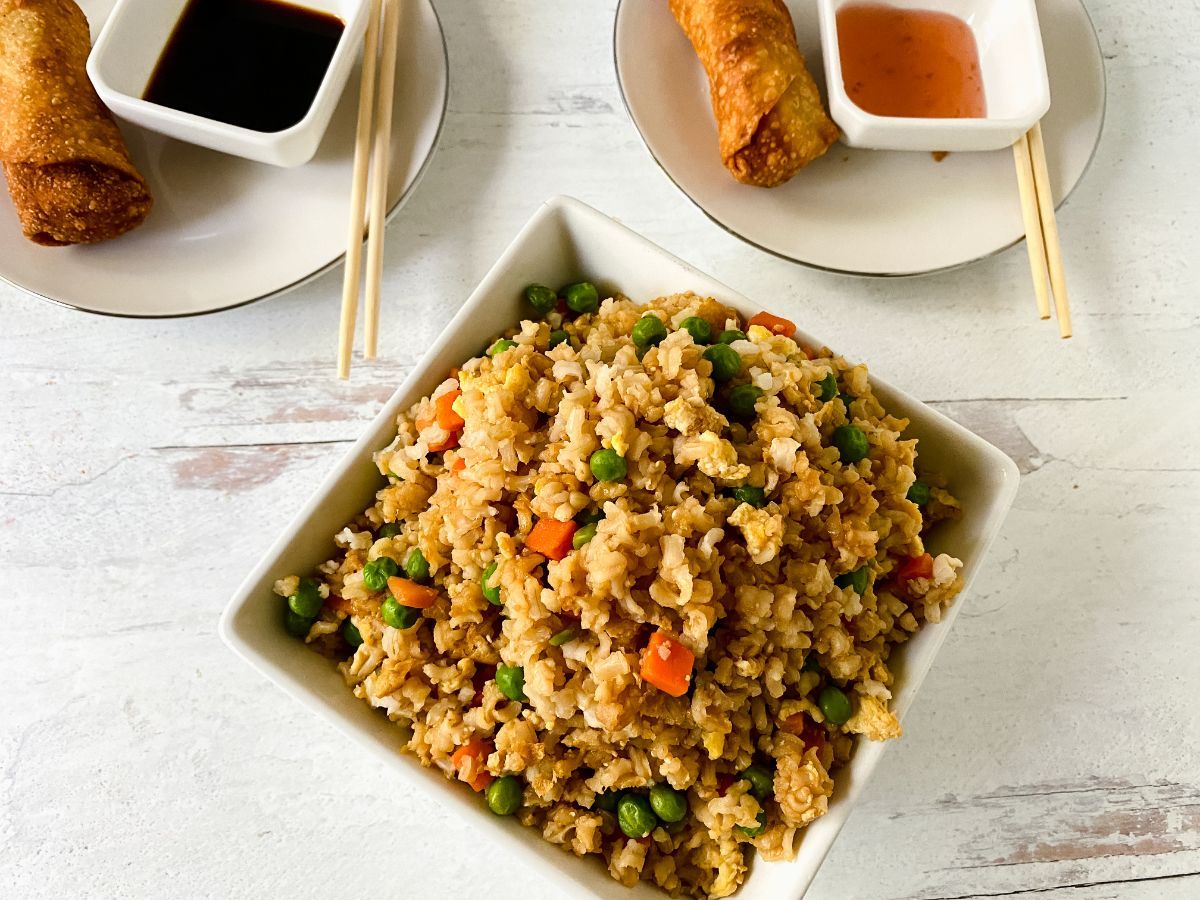 bowl of fried rice by two saucers holding egg rolls and sauces