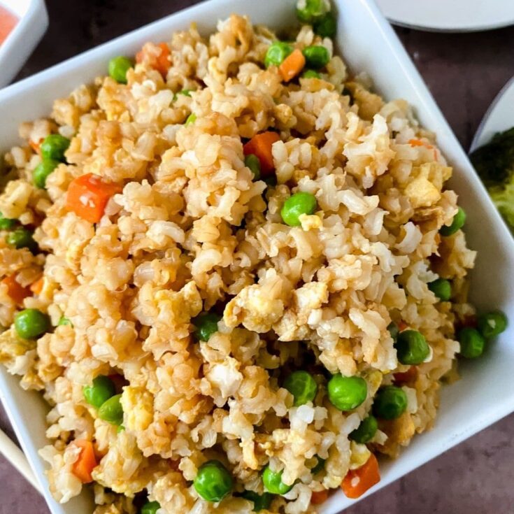 square white bowl of fried rice next to saucers of chicken and vegetables