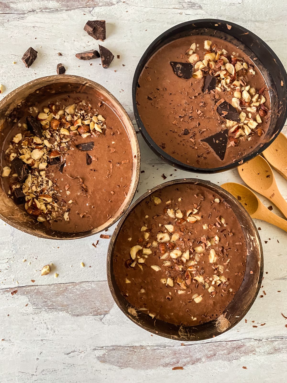 three large bowls filled with chocolate topped with hazelnuts on table