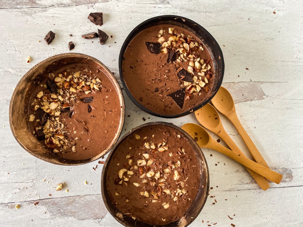 bowls of smoothie on marble table by wood spoon with cocoa bits on top