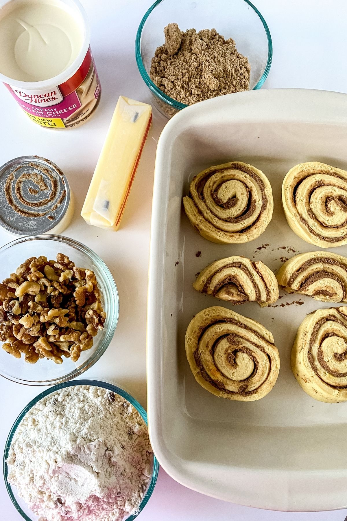 unbaked cinnamon rolls in baking dish next to ingredients in glass bowls