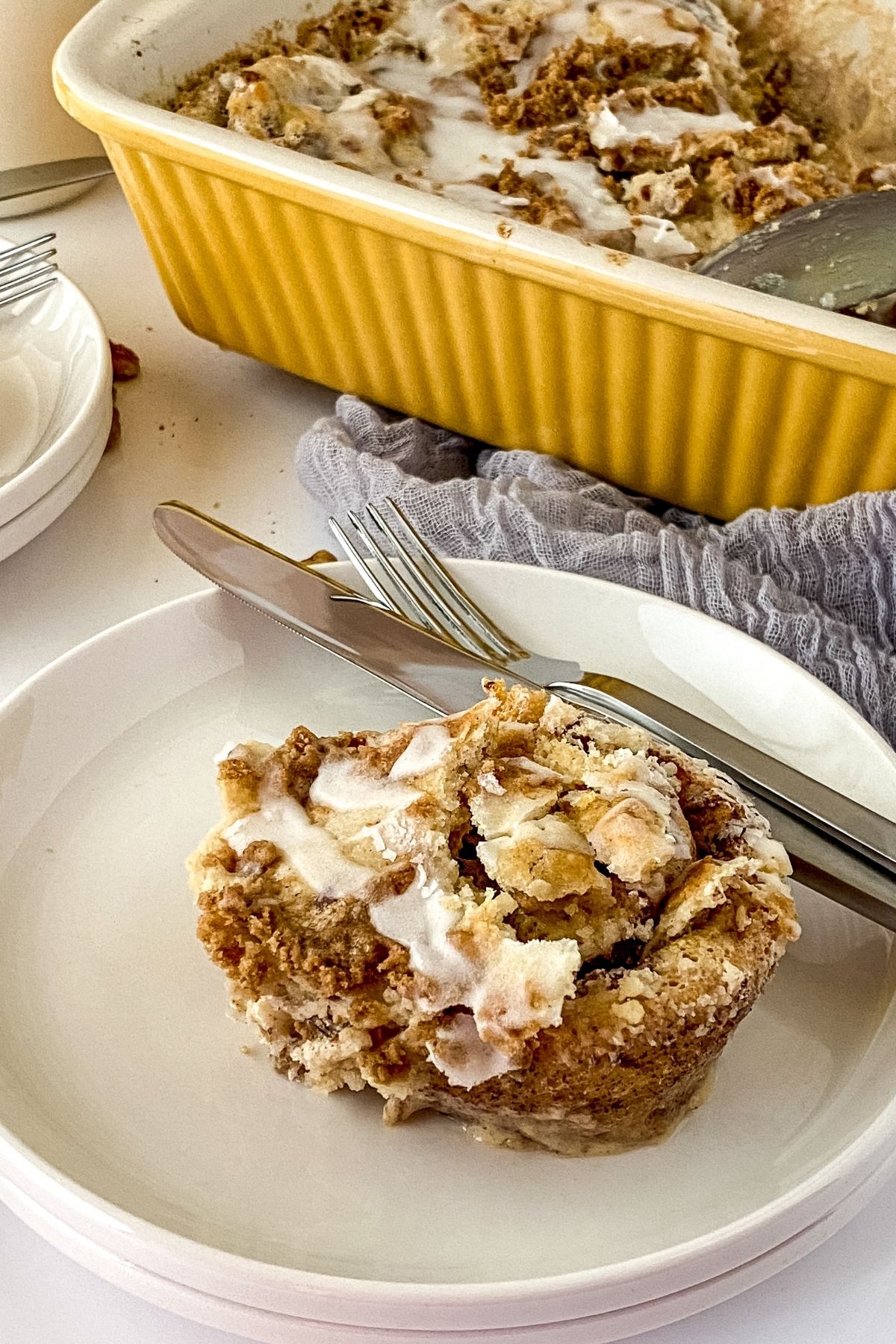 slice of cinnamon roll cake on white plate by yellow baking dish and blue napkin