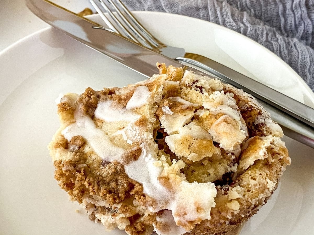 slice of cinnamon roll cake on white plate with fork and knife