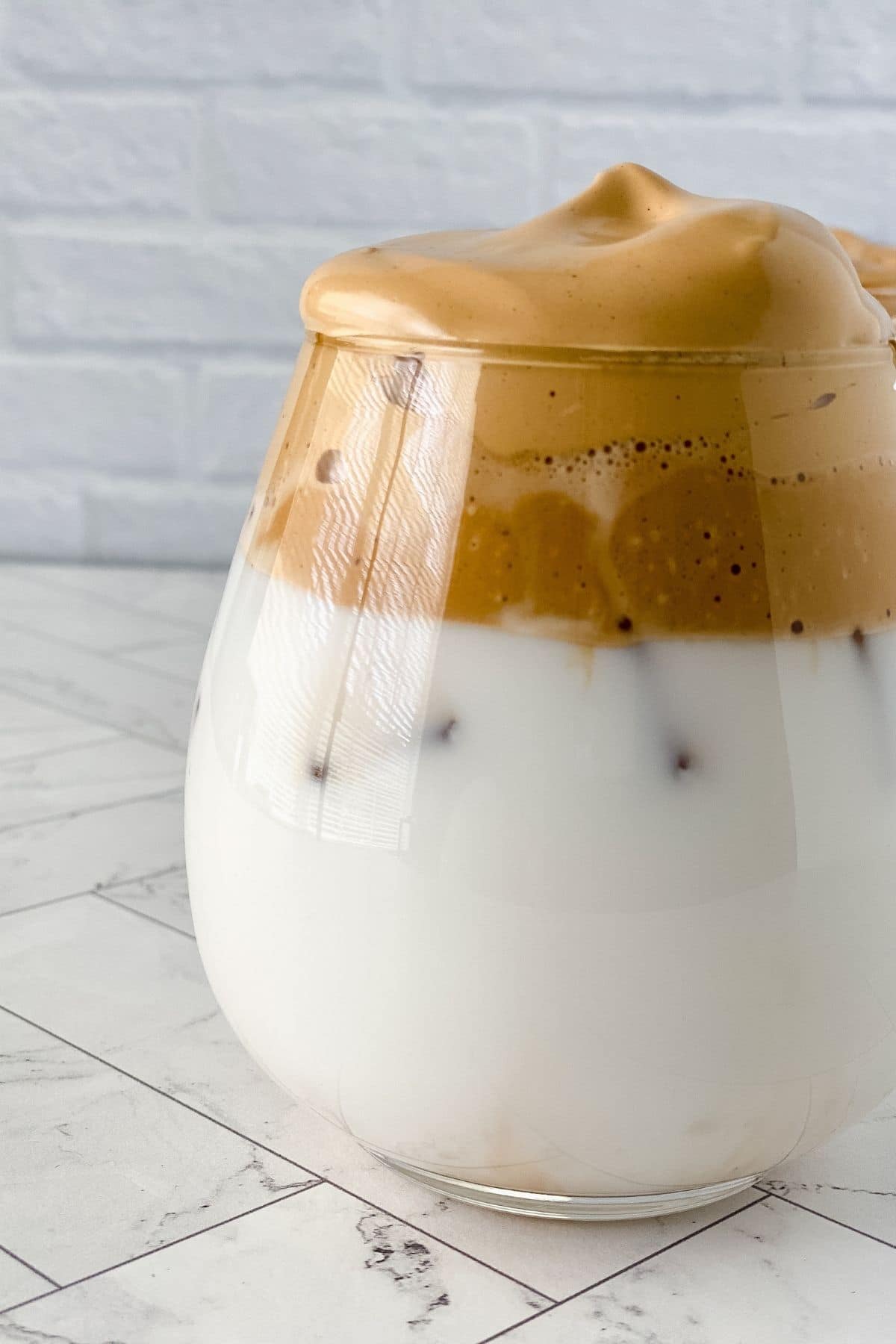short glass of milk with whipped coffee sitting on tiled surface