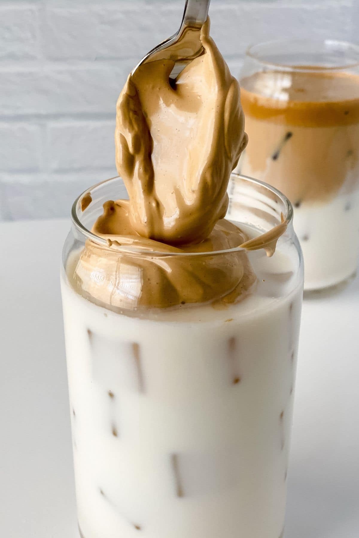 spoon of whipped coffee held above glass of milk with ice