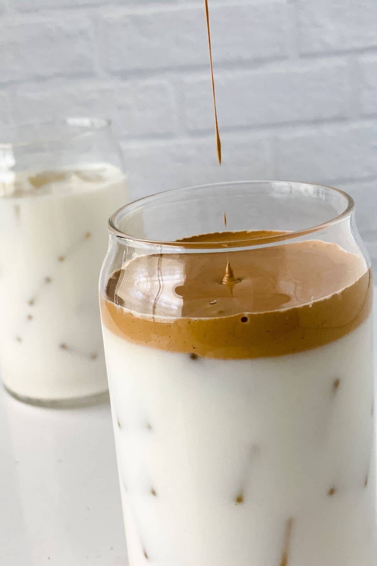 coffee dripping down into glass with milk and whipped coffee