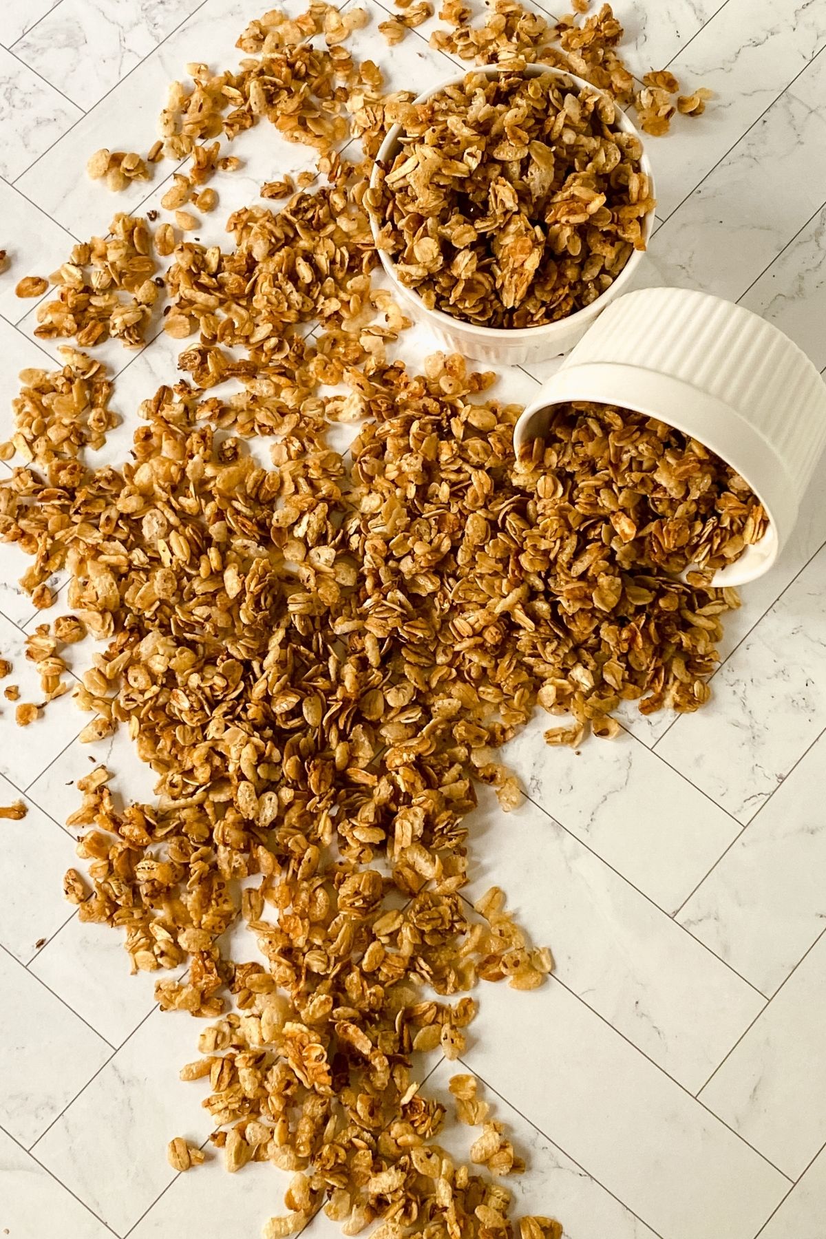 two white bowls of granola spilling onto tiled table