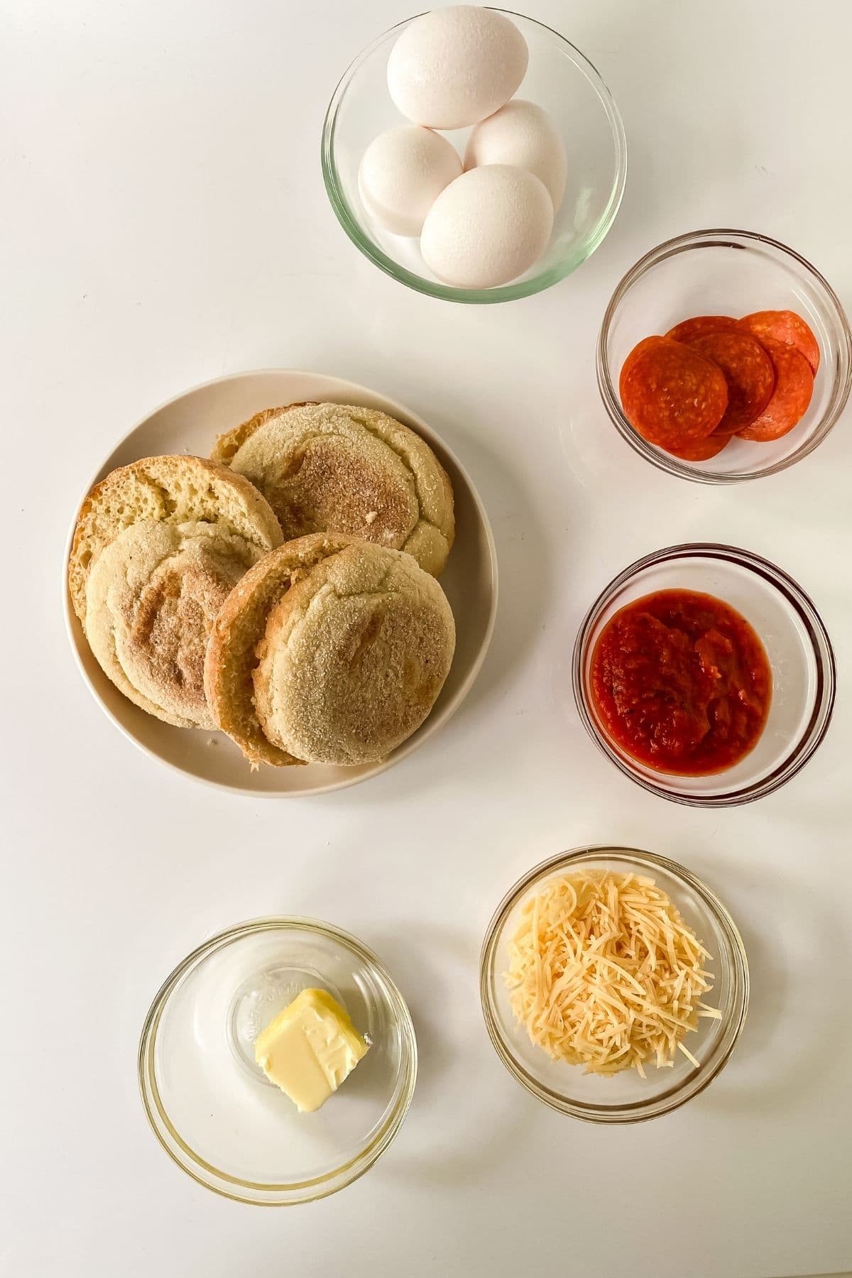 english muffin and glass bowls of sauce and cheese on white table