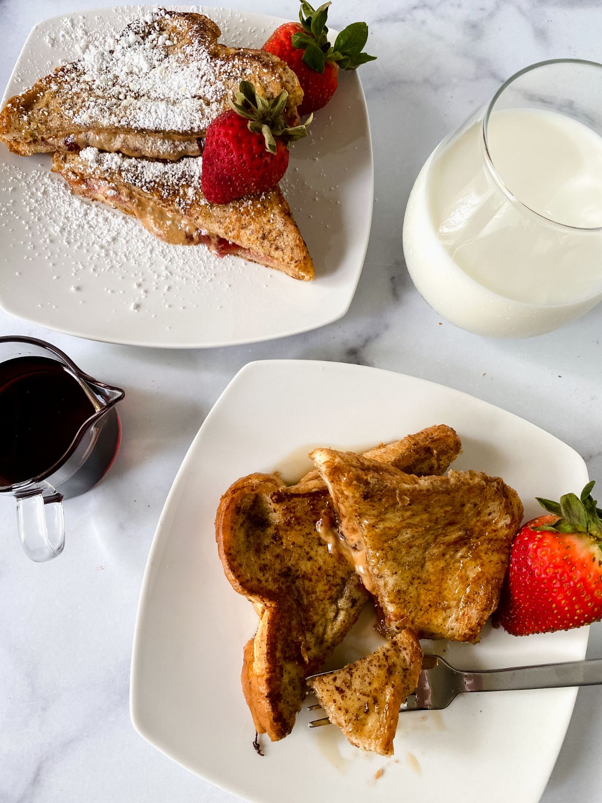 two square white plates of french toast with strawberry and glass cup of milk