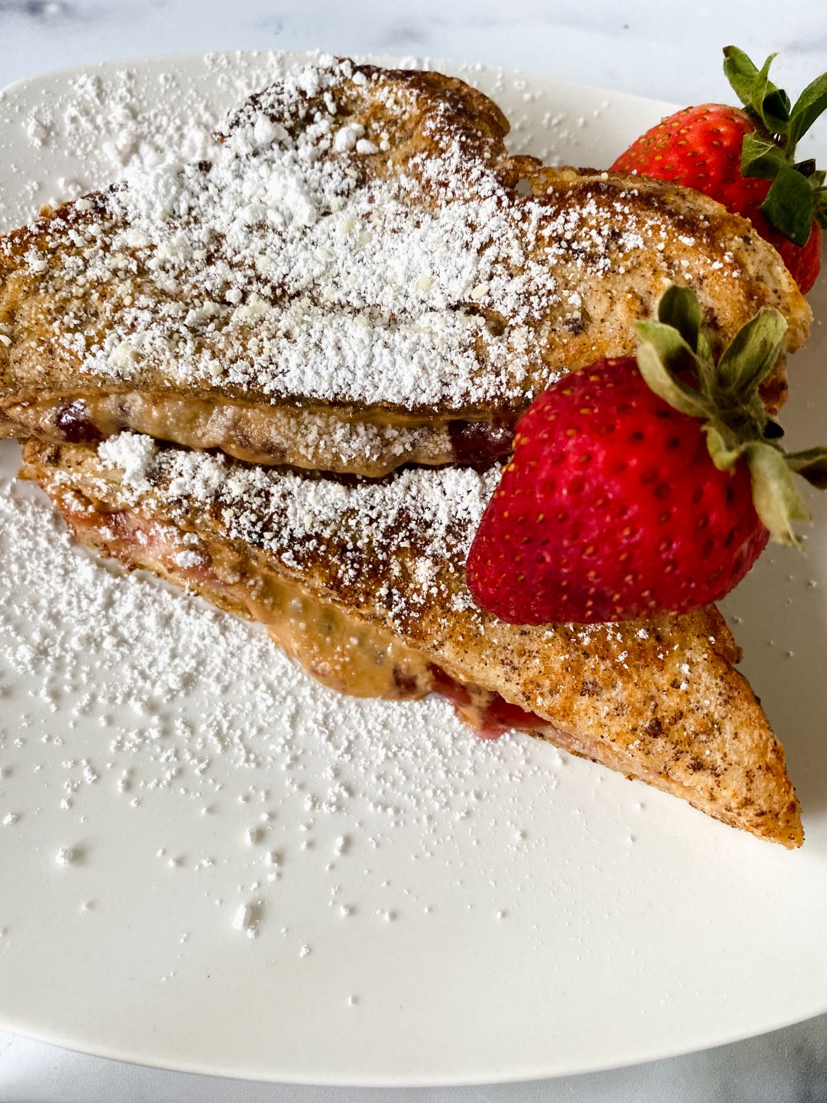 two slices of toast on white plate topped with powdered sugar and berry