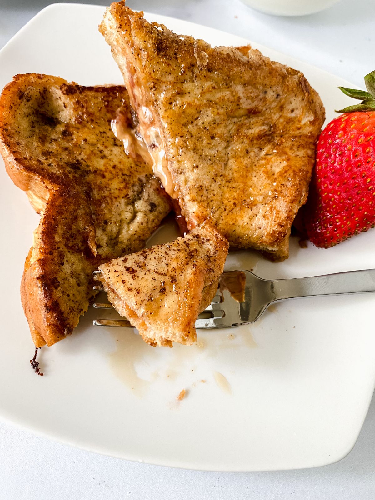bite of french toast on fork sitting on white plate