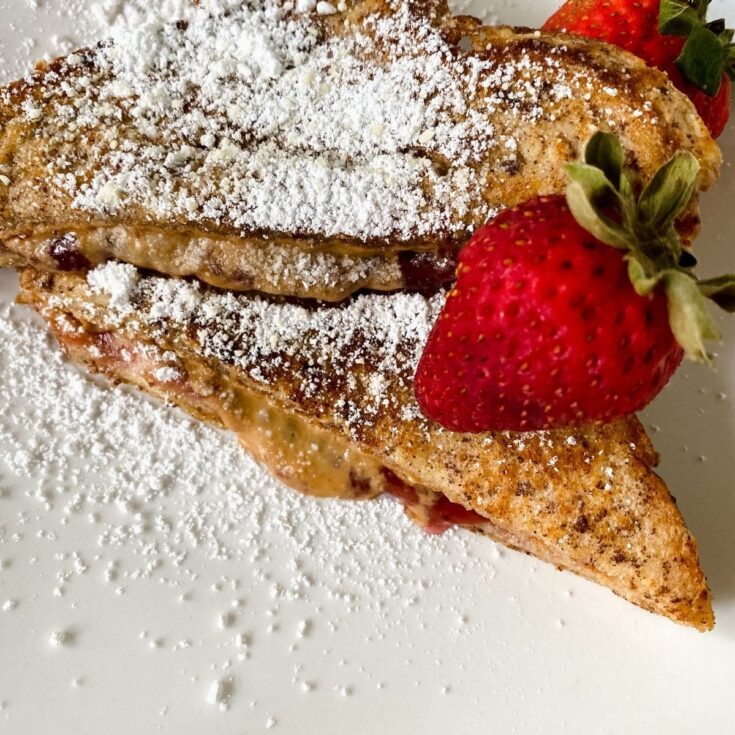 two slices of toast on white plate topped with powdered sugar and berry