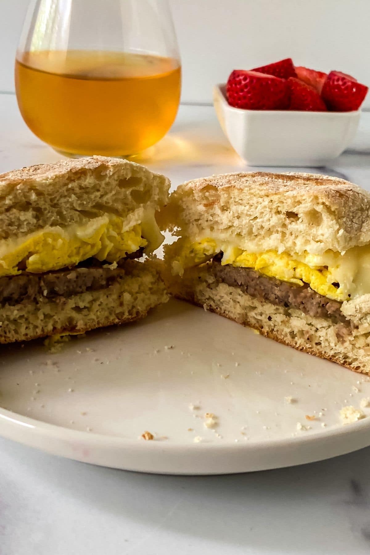 breakfast sandwich with sausage cut in half on white plate with juice in background