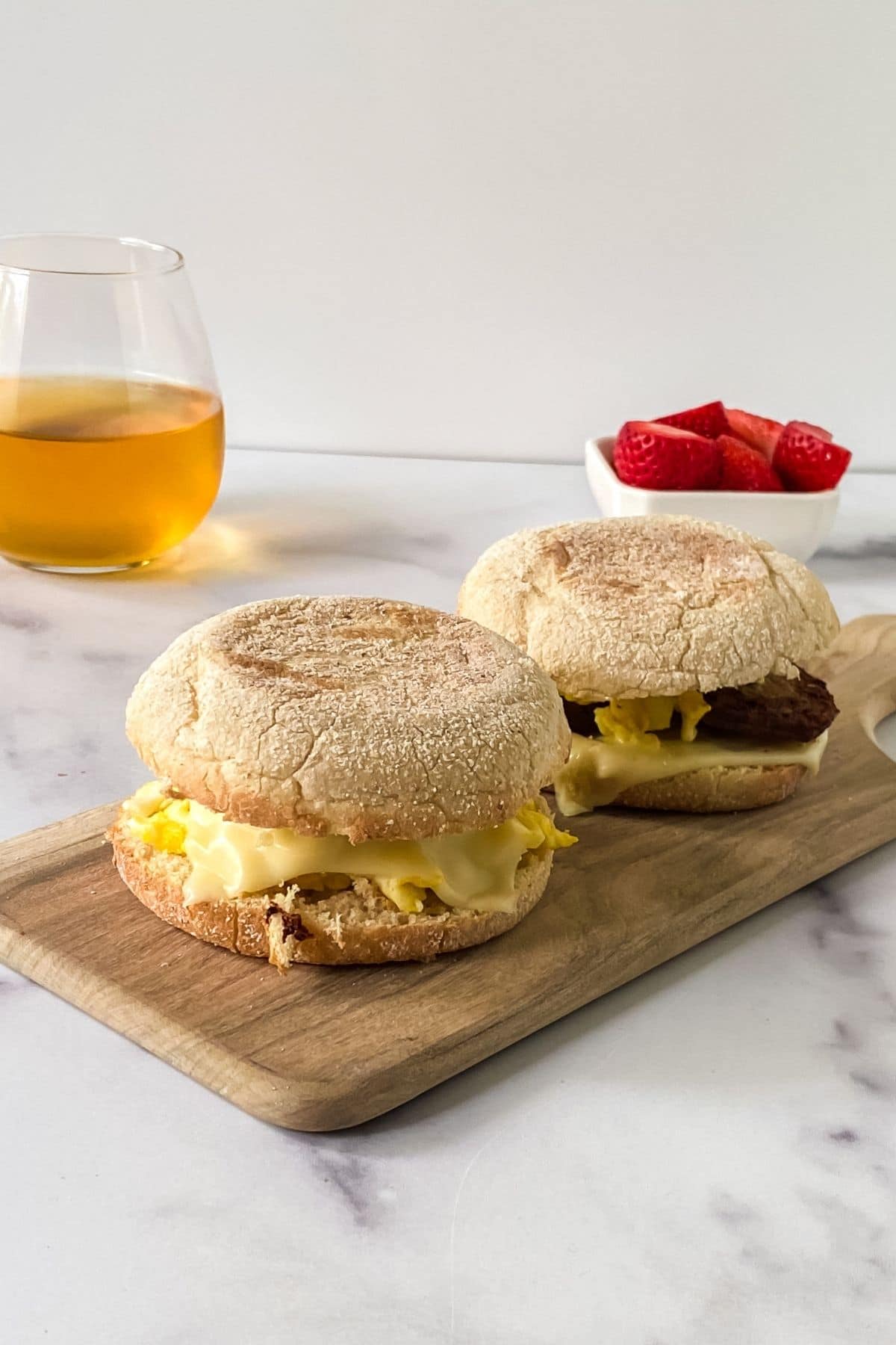 two McMuffins on board on table by small glass of juice