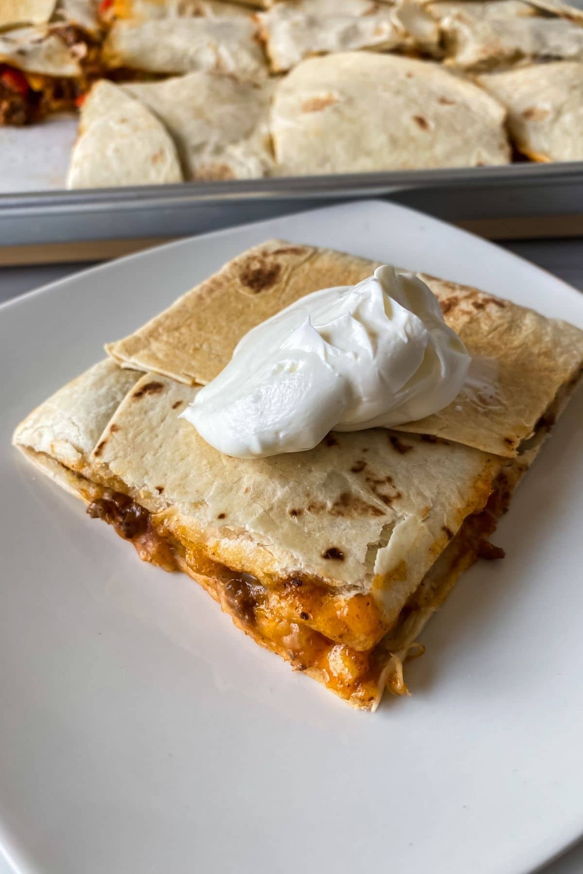 cheese beef quesadilla on white table with sour cream on top