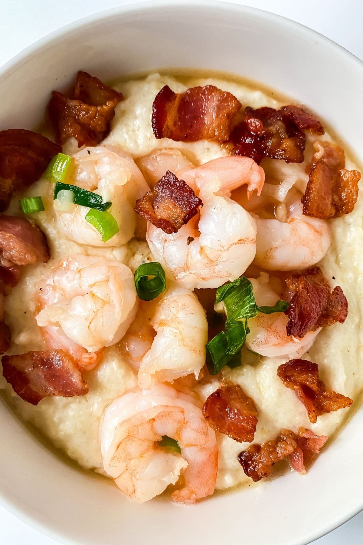 overhead image looking down on white bowl of shrimp and grits with bacon and green onion