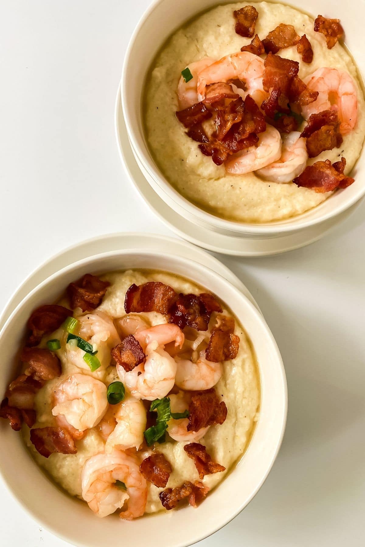 two white bowls of shrimp and grits on white table