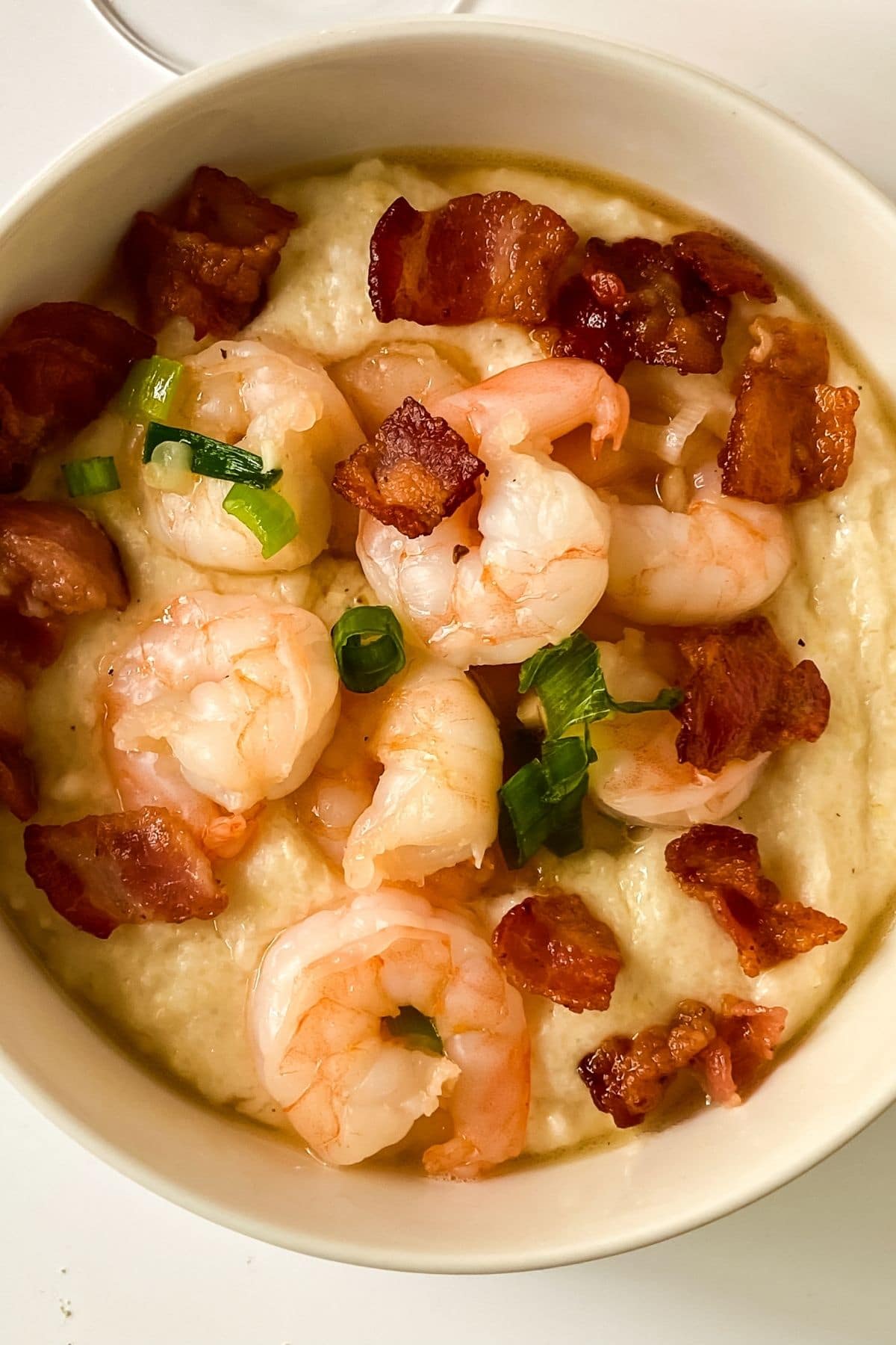 large cream bowl of grits topped with cooked shrimp and bacon