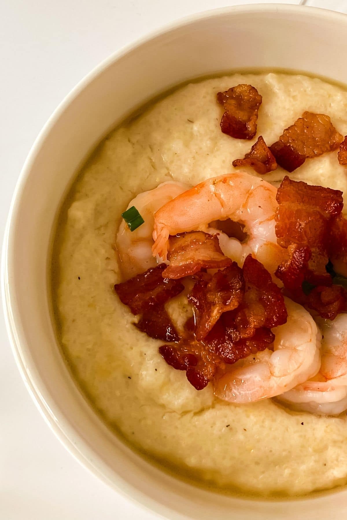cream bowl of grits topped with cooked shrimp and bacon