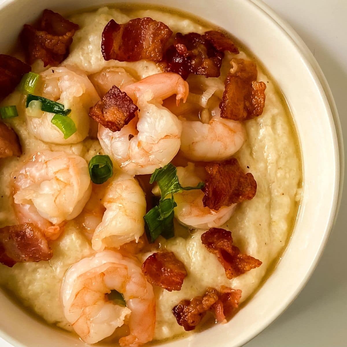 white bowl of grits topped with shrimp and bacon crumbles