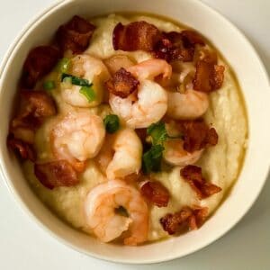 white bowl of grits topped with shrimp and bacon crumbles