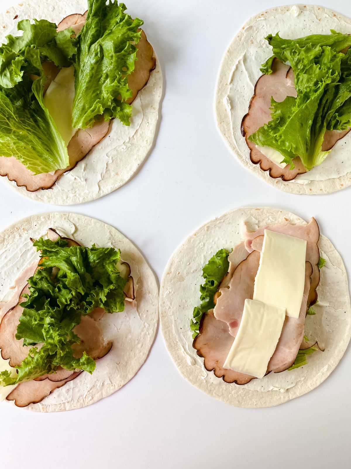 four tortillas on white table with lettuce cheese and turkey on top