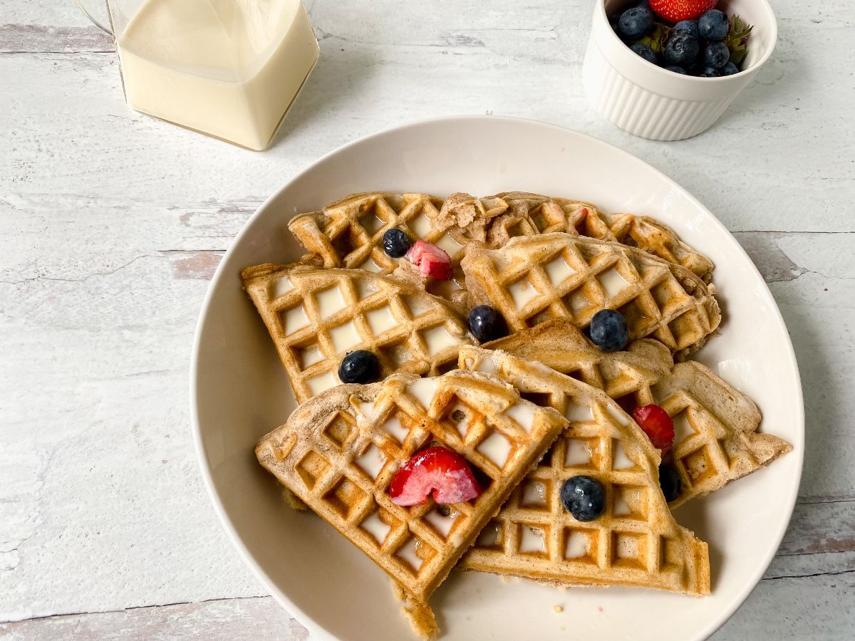 waffles on round white plate topped with syrup and berries