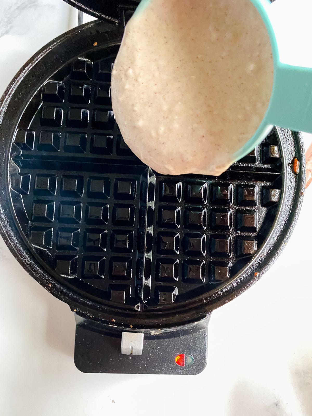 teal cup pouring waffle batter into waffle maker