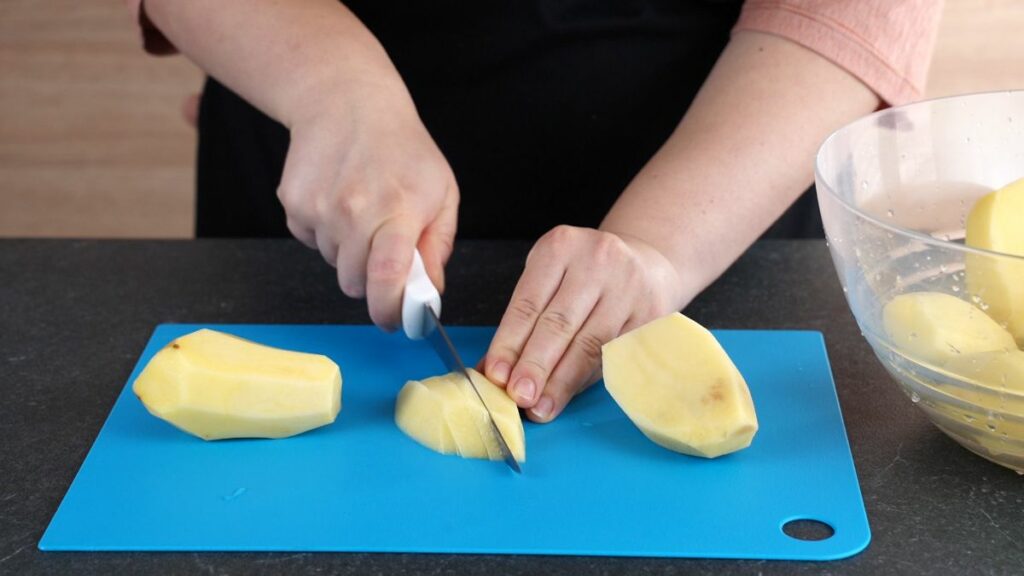 hand slicing potato into pieces on blue cutting board