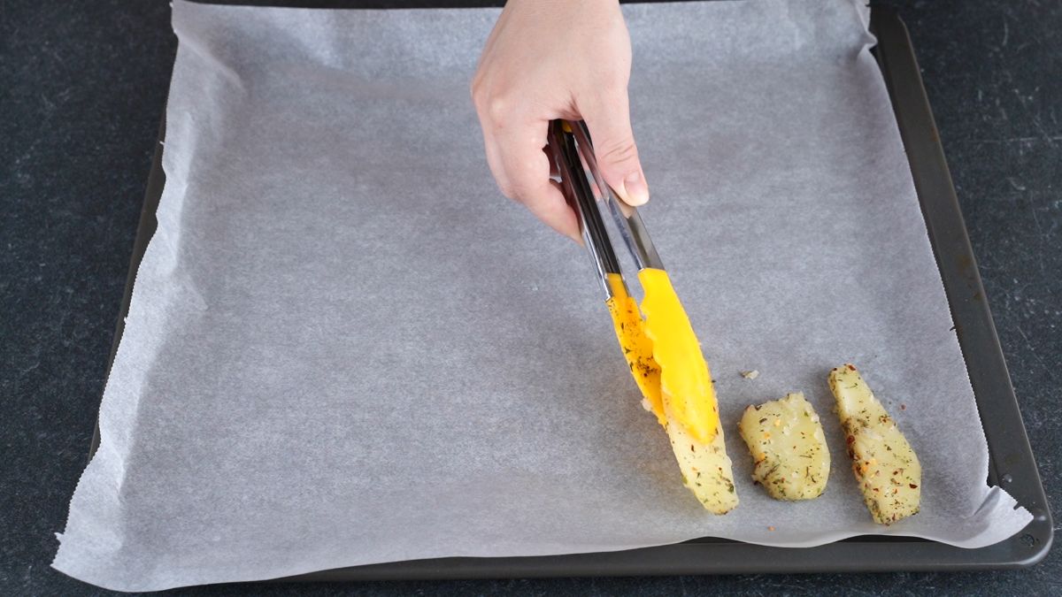 yellow tongs putting potato on baking sheet