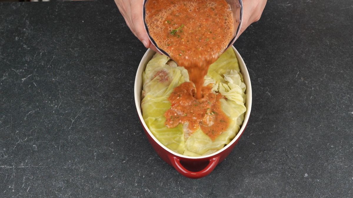 sauce being poured over the top of cabbage in casserole dish